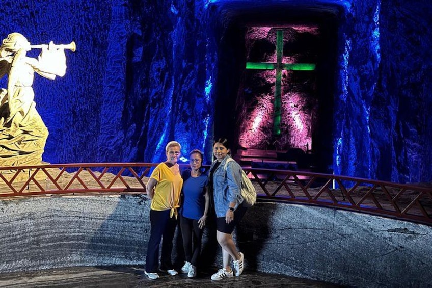 A cave-like structure with a statue of a figure playing a trumpet, a green cross, and a railing. 5