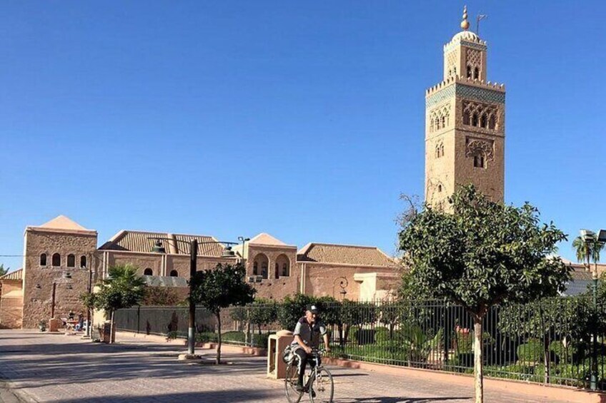A historic building with a prominent tower, a cyclist on the street, and a clear blue sky. 1