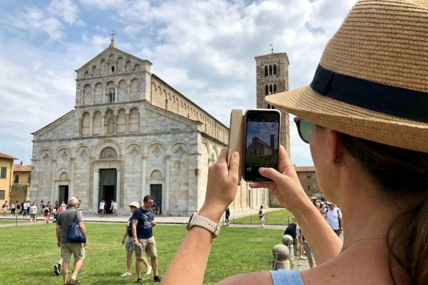 A historic church with a bell tower, tourists taking photos, and a grassy area in the foreground. 3