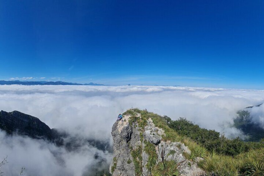 A mountain peak with a person standing on top, surrounded by clouds and greenery. 5