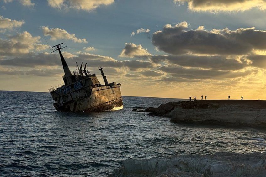 A sunken ship on a rocky shore with people standing on the cliff. 4
