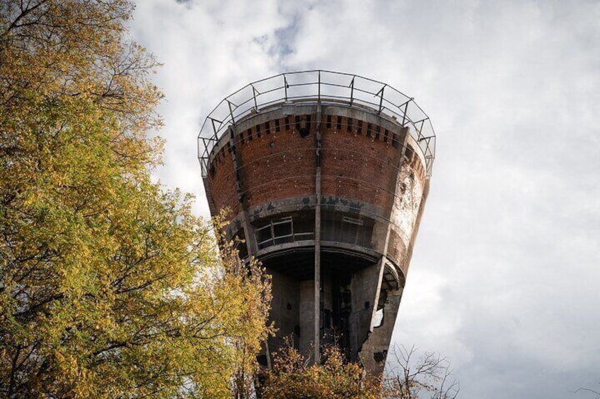 A tall, cylindrical brick water tower with a metal railing at the top, surrounded by autumn foliage. 1
