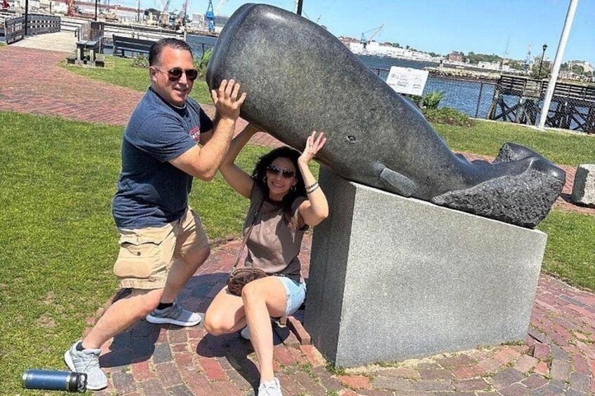 A man and a woman interacting with a whale sculpture in a park. 3