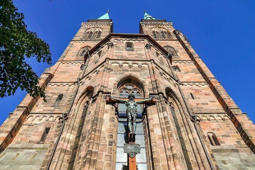 Een hoge bakstenen kerk met een standbeeld ervoor, twee torens en een helderblauwe lucht. 3