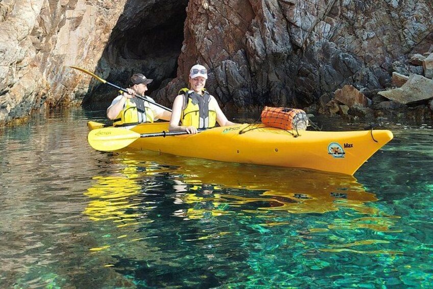 Two people kayaking in a yellow kayak on clear water with a rocky cave in the background. 5