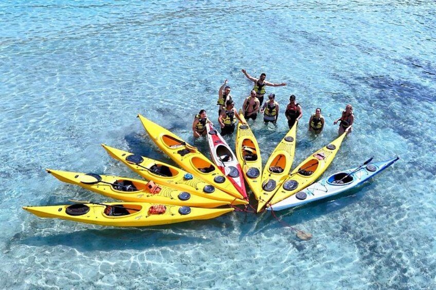 A group of people standing on a beach with kayaks arranged in a semi-circle. 4