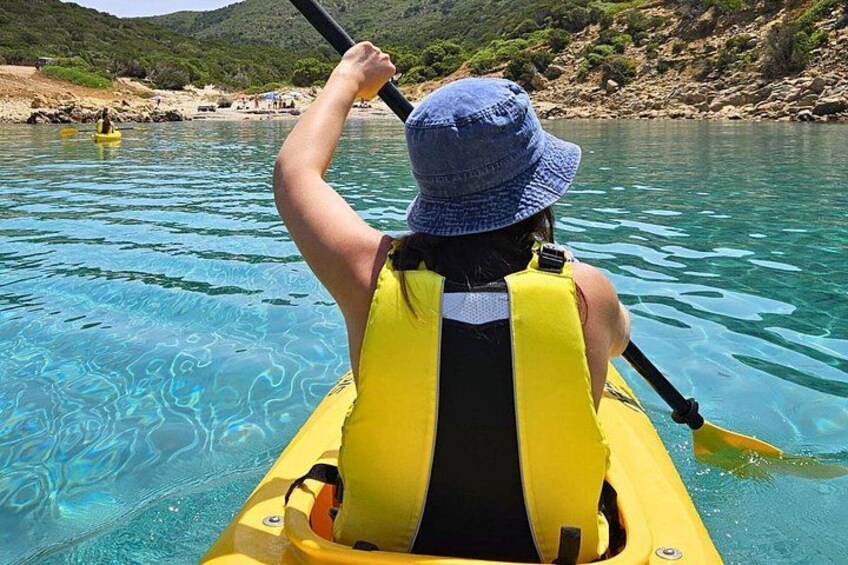 A person in a yellow kayak on clear blue water, wearing a blue hat and a yellow life jacket. 3