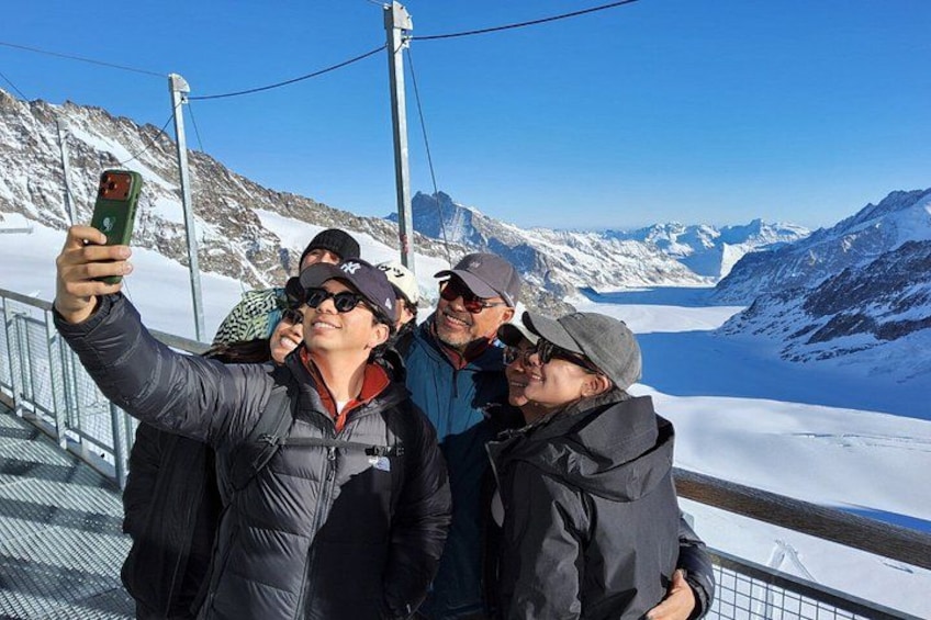 En gruppe mennesker tager en selfie på en sneklædt bjergsti under en klar himmel og et snedækket landskab. 3