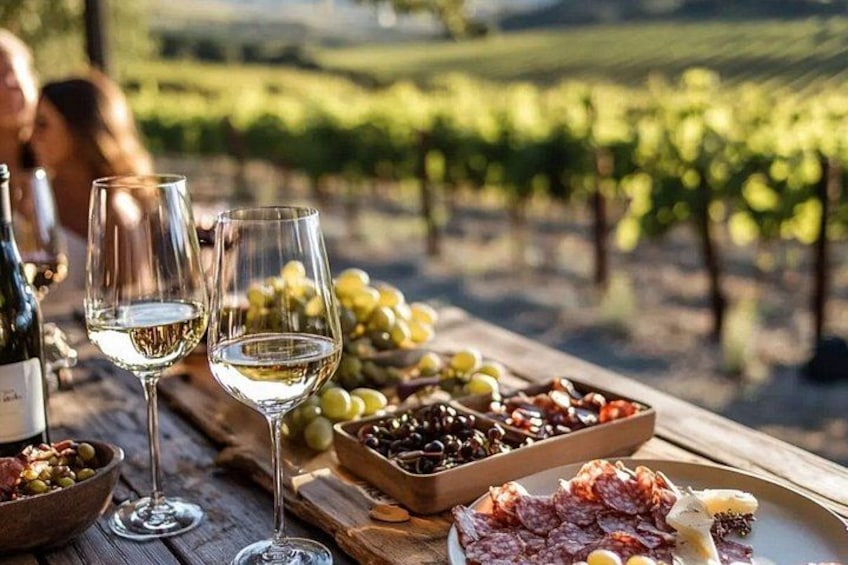 Un tavolo con bicchieri da vino, un tagliere di formaggi e grappoli d'uva in un vigneto. 4
