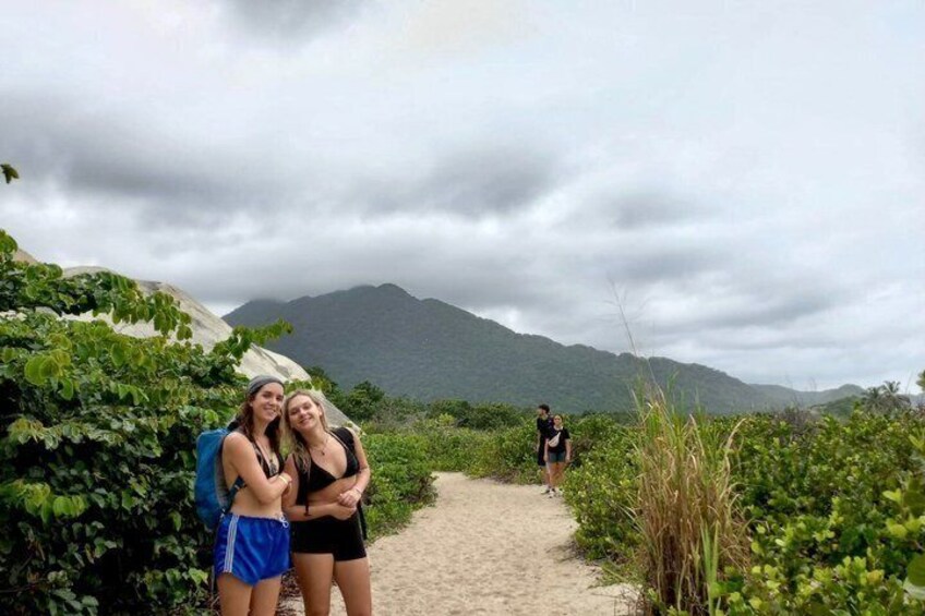 Two people hugging on a sandy path with greenery and mountains in the background. 2