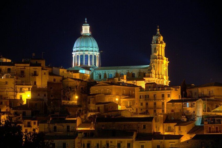 Paesaggio urbano notturno con edifici illuminati, una cupola imponente e un campanile. 1