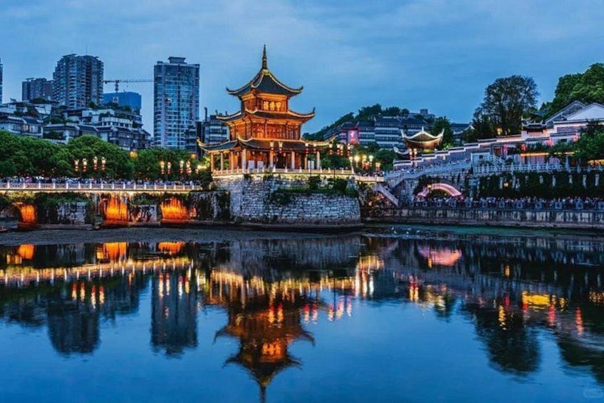 A traditional Chinese pagoda with a reflection in the water, surrounded by modern buildings and a stone bridge. 1