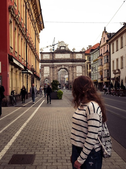 A pedestrian street lined with historic buildings, a large archway, and people walking. 3