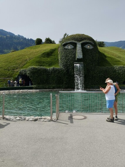 A large hedge sculpture of a face, a fountain, and a body of water. 2
