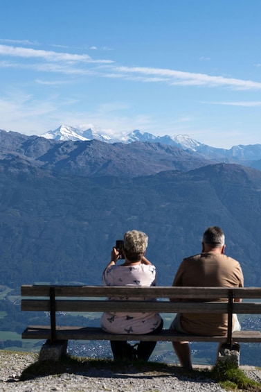 Two people sitting on a bench overlooking a mountainous landscape with snow-capped peaks. 1