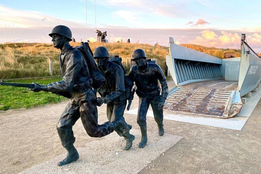 A military statue of soldiers marching, a large aircraft, and a grassy field. 1
