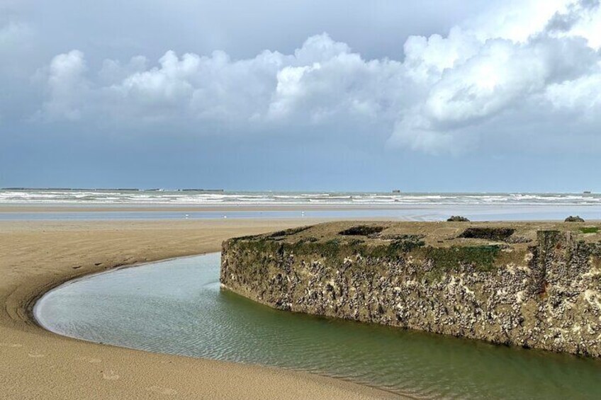 Una playa con un muro de piedra curvado y agua tranquila. 2