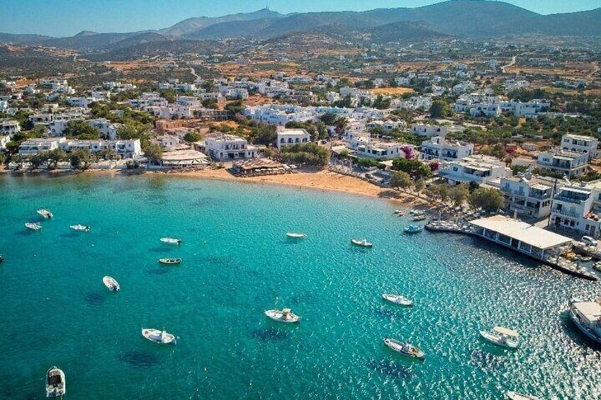 A coastal town with white buildings, a beach, and boats on turquoise waters. 4