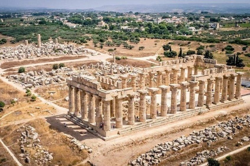 An ancient Greek temple with columns, ruins, and a surrounding landscape. 1