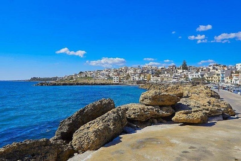 A coastal town with a rocky shoreline, clear blue sea, and buildings along the coast. 3