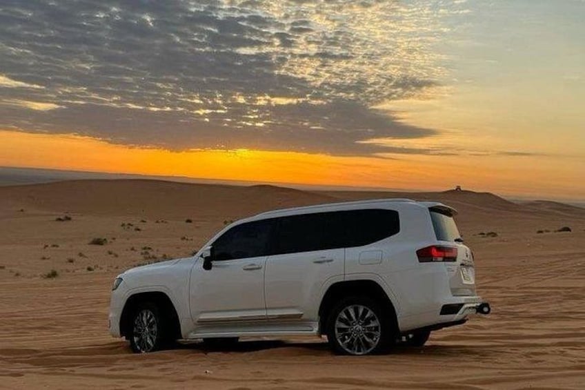 A white SUV parked on a desert dune during sunset. 2