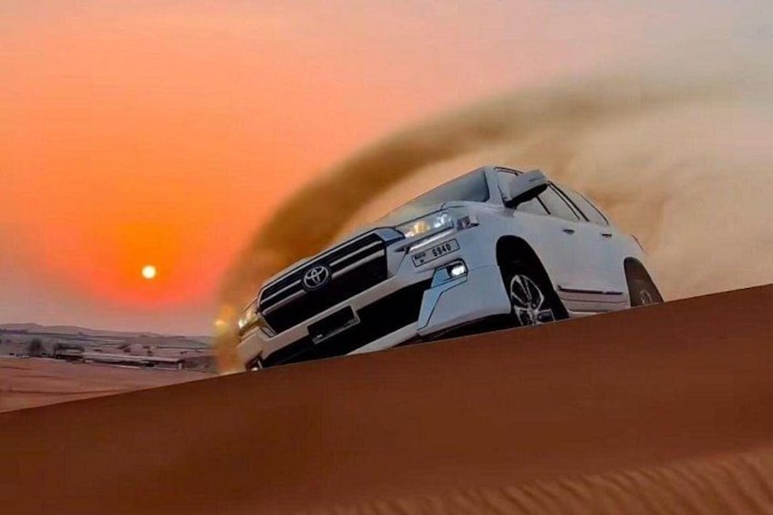 A white car driving on a sandy surface with a sunset in the background. 1