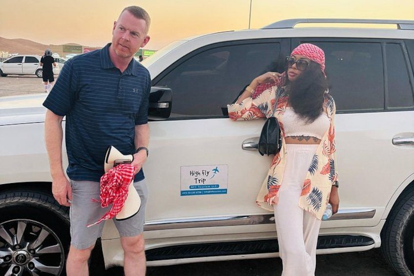 A man and a woman standing next to a white SUV with a sign on the door. 3