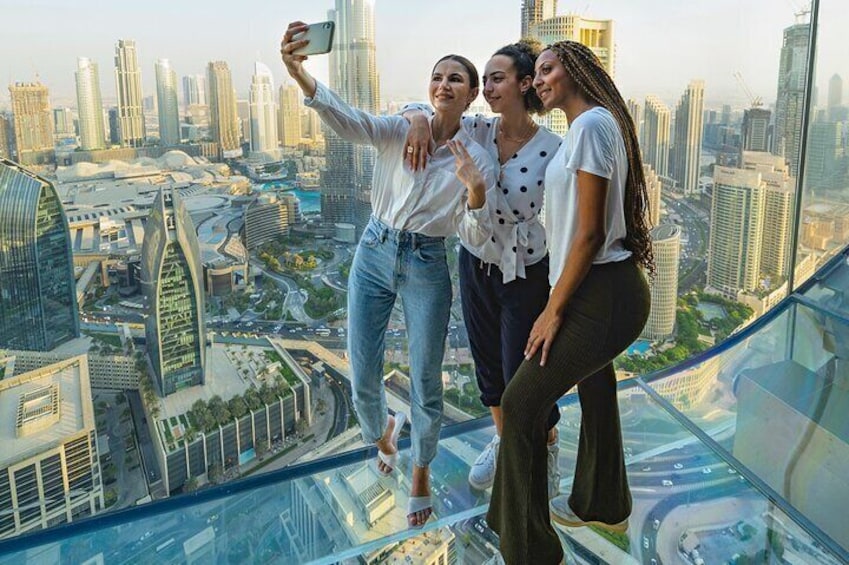 Three people taking a selfie on a glass balcony with a cityscape in the background. 1