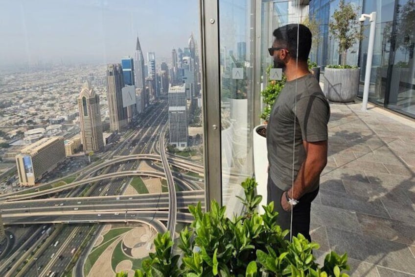 A man standing on a balcony overlooking a cityscape with tall buildings and a complex highway system. 2