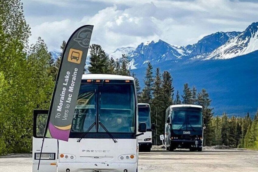 Un autobus arborant un panneau indiquant « Vers le lac Moraine » est garé sur une route, avec des montagnes en arrière-plan. 1