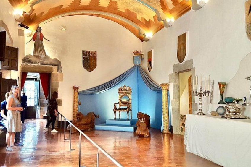 Une pièce avec un fond bleu drapé, une chaise en bois et une table sur laquelle se trouve un chandelier. 4