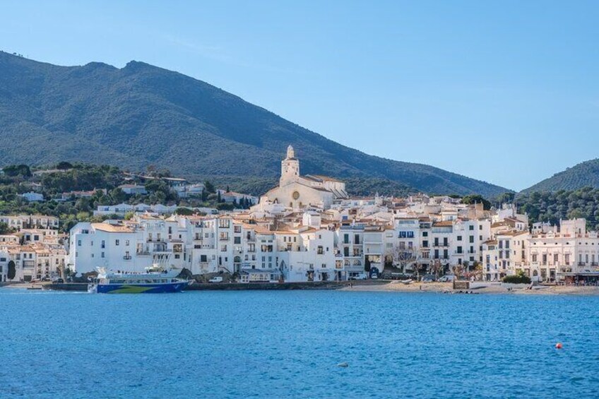 Un pueblo costero con edificios blancos, una iglesia destacada y una montaña al fondo. 2