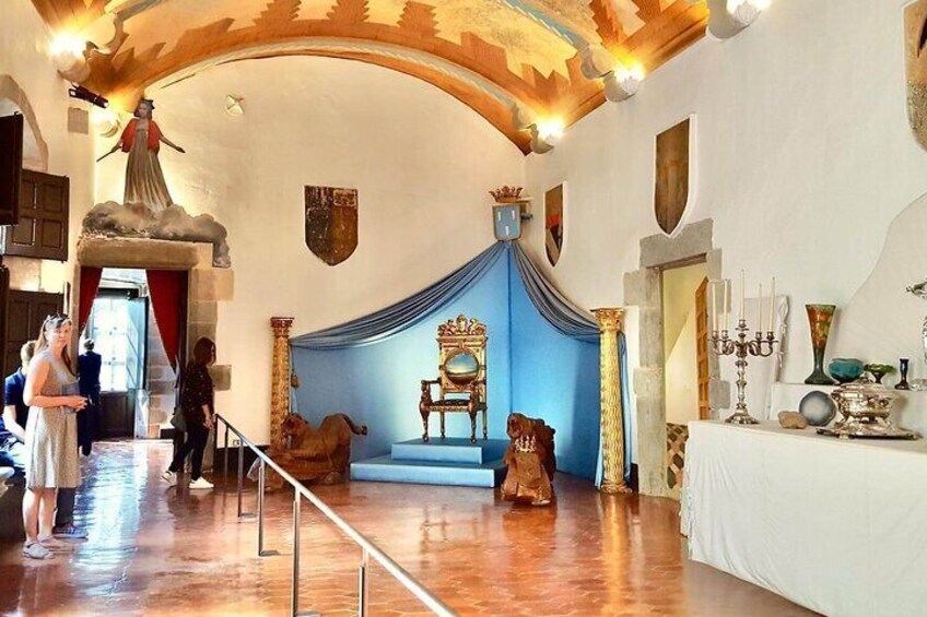 Un interior histórico con un fondo azul con cortinas, un trono y una estatua de mujer. 4