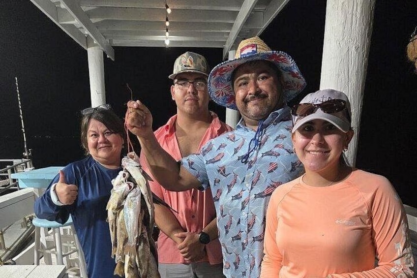 A group of people on a boat with fishing rods, a boat, and a dock. 2