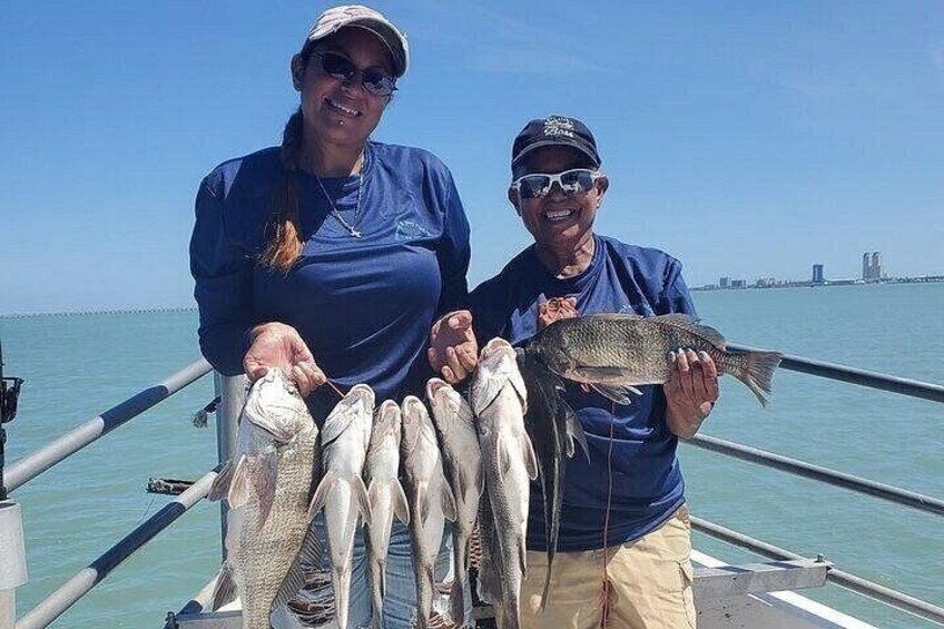 Two people holding fish on a boat with a clear sky and water in the background. 2