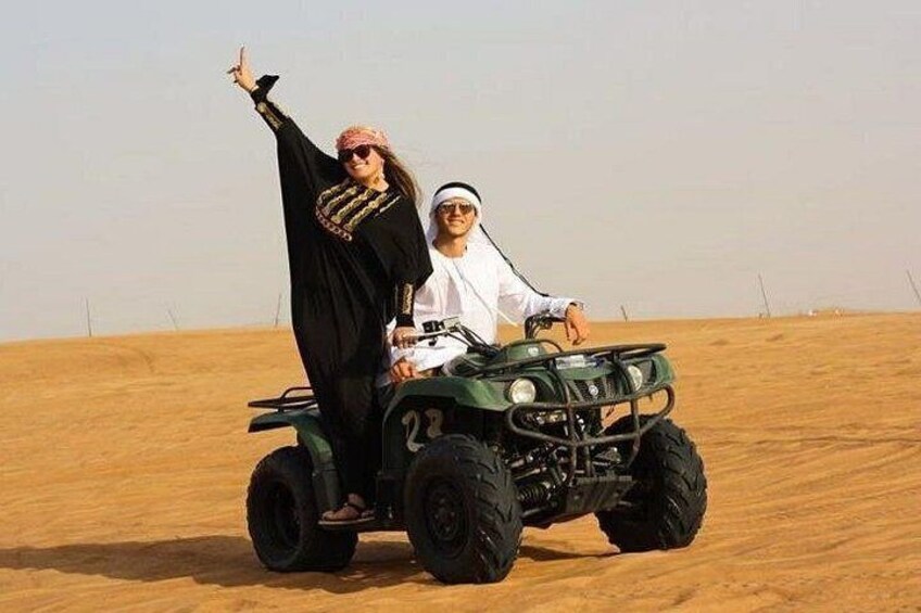 Two people on a green off-road vehicle in a desert with sand dunes. 4