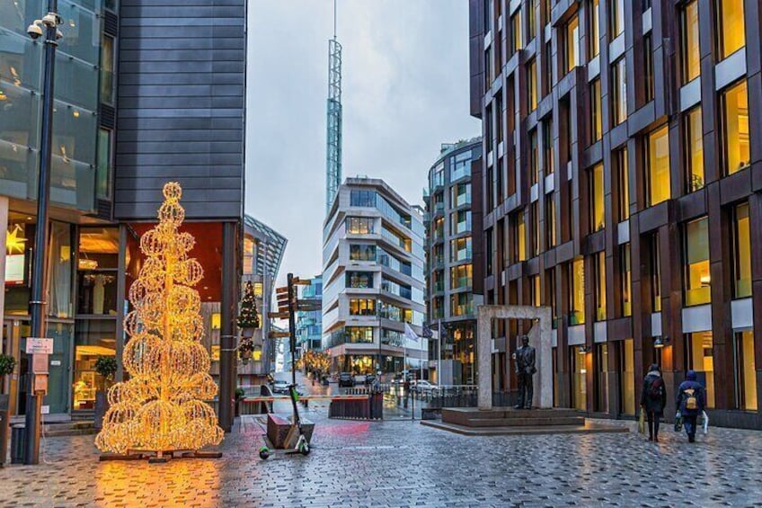 A city square with a large illuminated Christmas tree, modern buildings, and a tall skyscraper in the background. 4