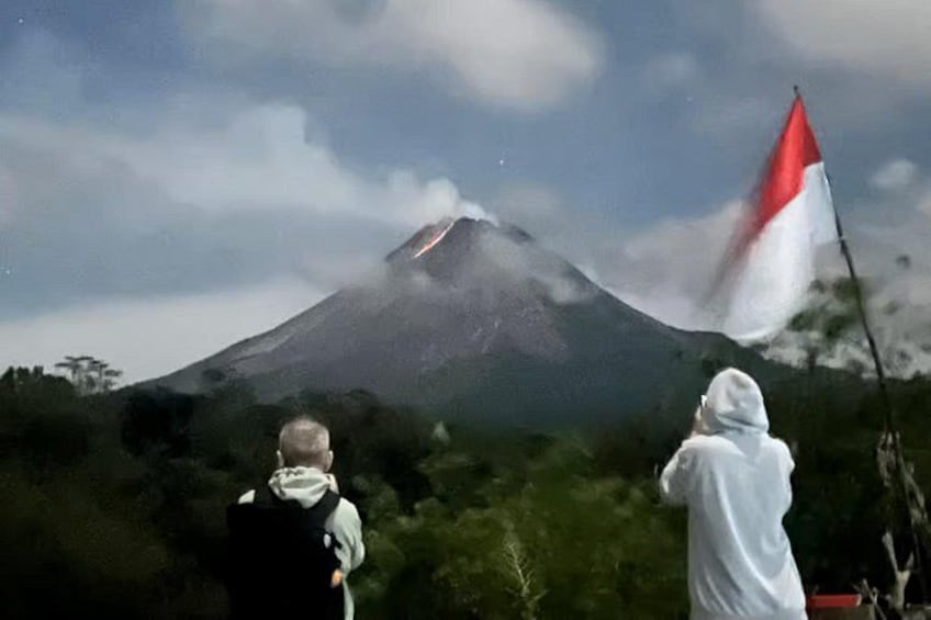 A volcano with smoke, a flag, and two people. 3