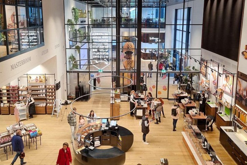 A spacious indoor shopping area with a central circular seating area, surrounded by various retail displays and a large windowed section in the background. 3