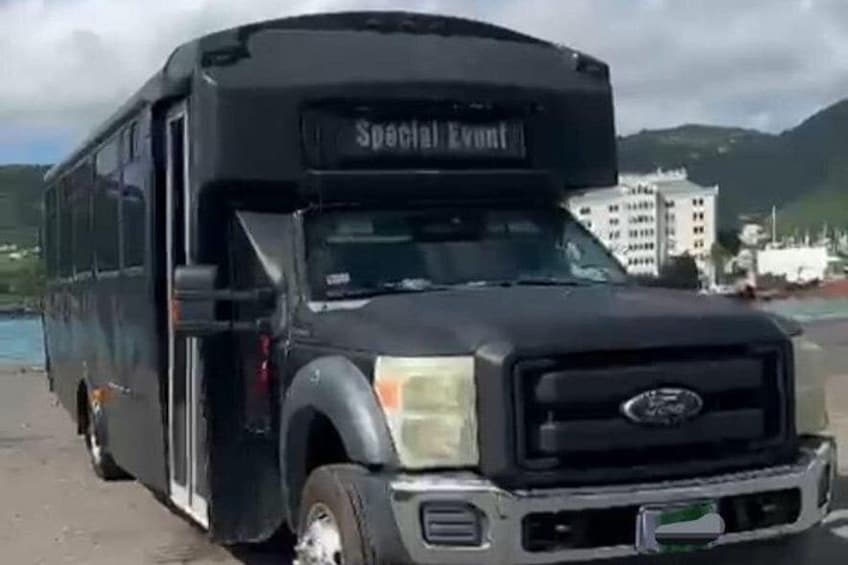 A black bus with 'Special Event' written on the front, parked near a body of water with buildings and hills in the background. 1