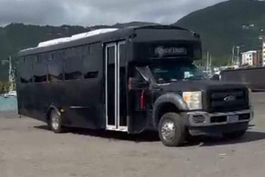 A black bus parked on a paved surface with a mountainous background. 2