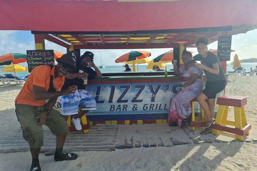 A beachside bar and grill named Lizzy's with a signboard, umbrellas, and beach chairs. 5