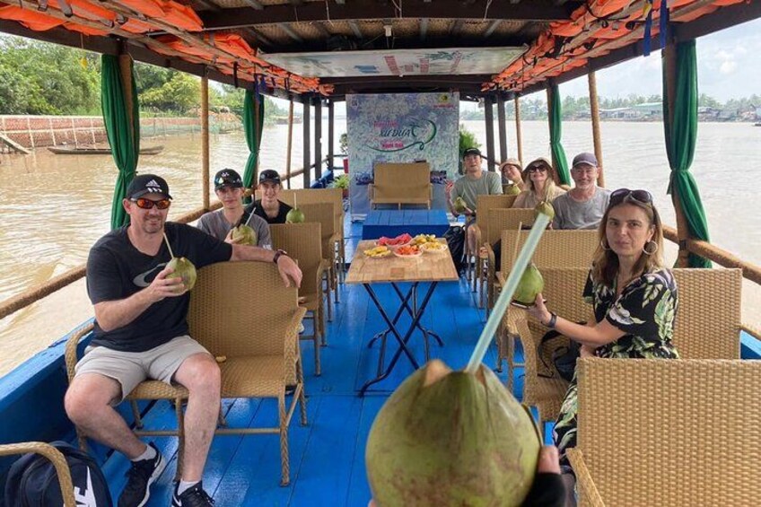 People on a boat with a table and chairs, a blue floor, and a covered area with green curtains. 2