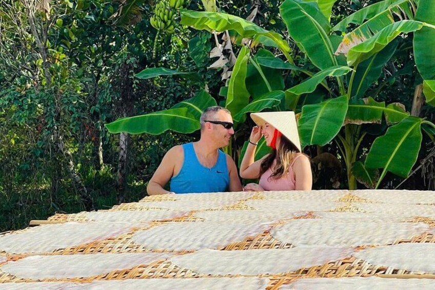 Two people sitting on a mat outdoors with a tropical background. 3