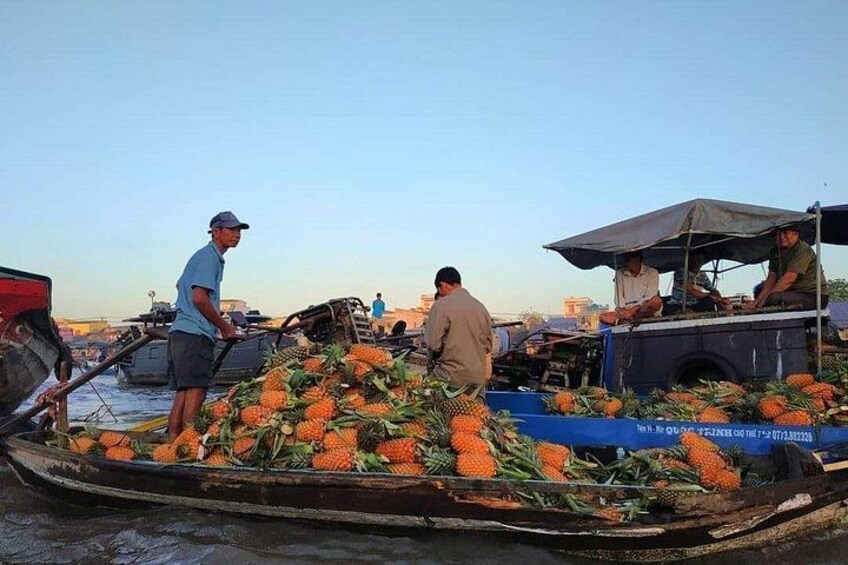 A boat loaded with pineapples, people on the boat, and a market scene in the background. 2
