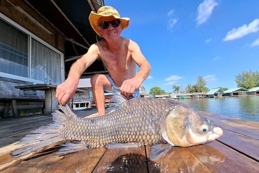 A person holding a large fish on a wooden dock. 2