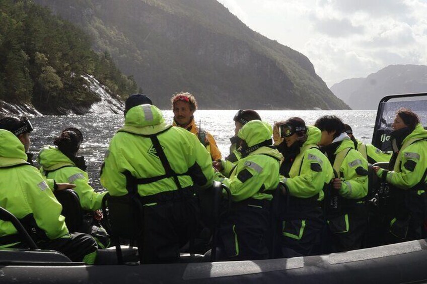 Un grupo de personas con chaquetas verde brillante en un barco cerca de una costa montañosa. 4
