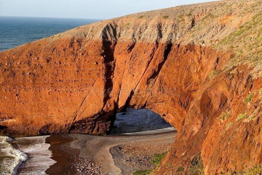 A coastal cliff with a natural arch formation, a beach, and the ocean. 4