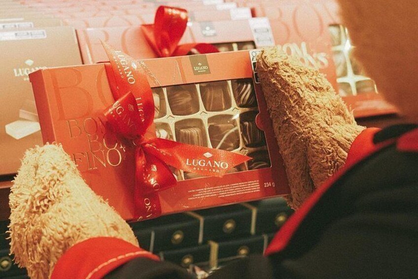 Una persona sostiene una caja de regalo con un lazo rojo, rodeada de otras cajas. 4