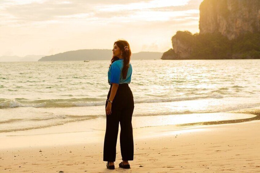 A person standing on a sandy beach with the ocean and a cliff in the background. 1
